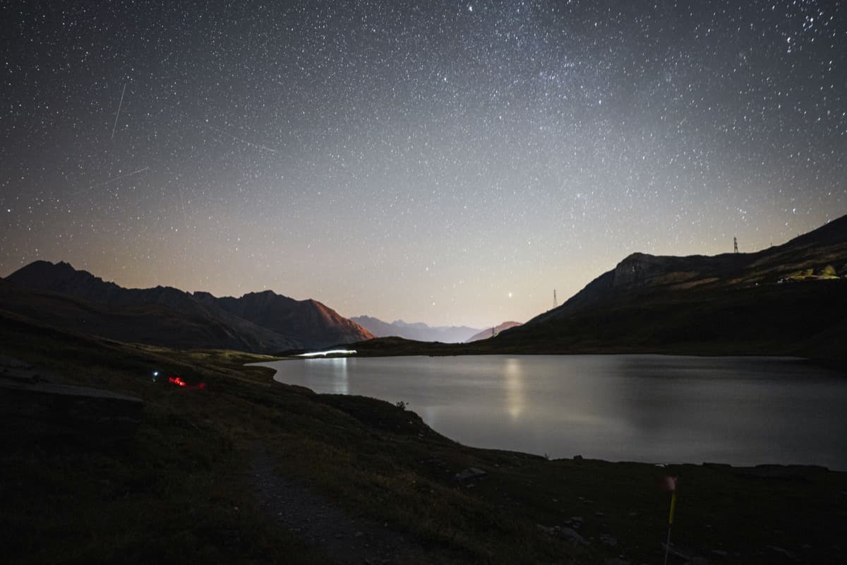 Starry night sky over a mountain lake with headlamp trails