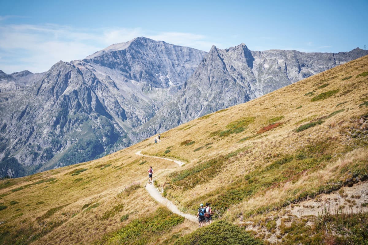 Runners on a winding ridgeline trail with dramatic peaks